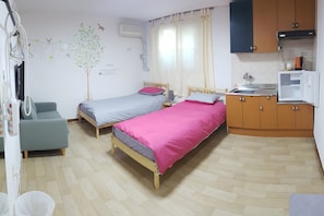 Une chambre avec deux lits simples, une petite kitchenette, un plancher en bois et un climatiseur fixé au mur.