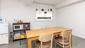 Een moderne keuken met een houten tafel en stoelen, een magnetron, een koelkast en een plank met diverse spullen.