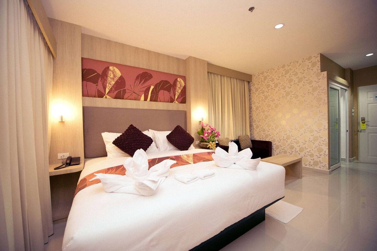 Habitación de hotel con una cama grande, una mesita de noche con teléfono, una obra de arte en la pared y un arreglo floral.