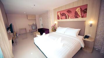 A hotel room with a large bed, a desk, a chair, a small table, a nightstand, and a wall-mounted artwork.
