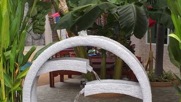 Uma fonte de pedra com água corrente, rodeada por plantas em vasos e um chão de azulejos.