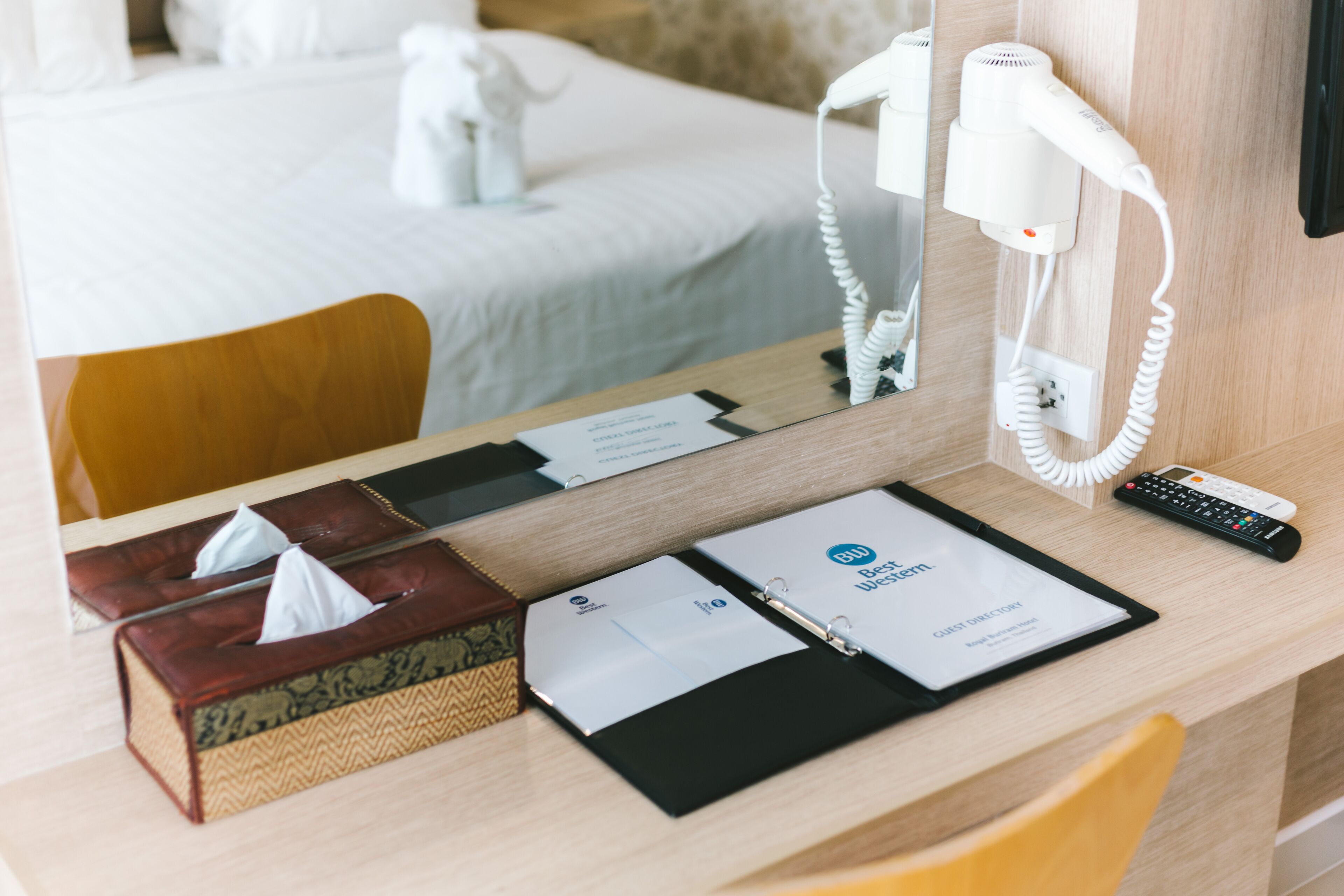 Habitación de hotel con escritorio de madera, espejo, secador de pelo, control remoto, caja de pañuelos y guía del huésped.