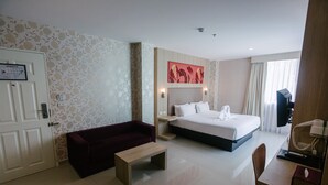 Habitación de hotel con cama, escritorio, silla, mesita pequeña, sofá y televisor.