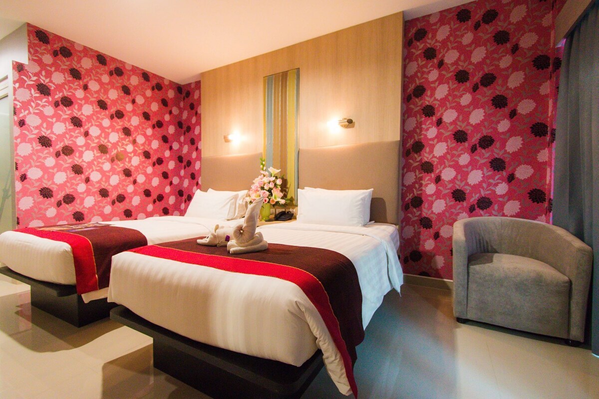 A hotel room with two beds, a sitting area with a chair, and a floral wallpaper design.