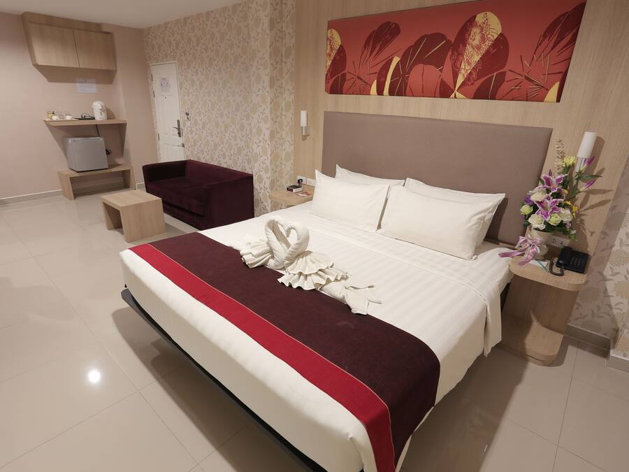 Habitación de hotel con una cama grande, un escritorio, una silla, un refrigerador pequeño, una mesita de noche y una obra de arte colgada en la pared.
