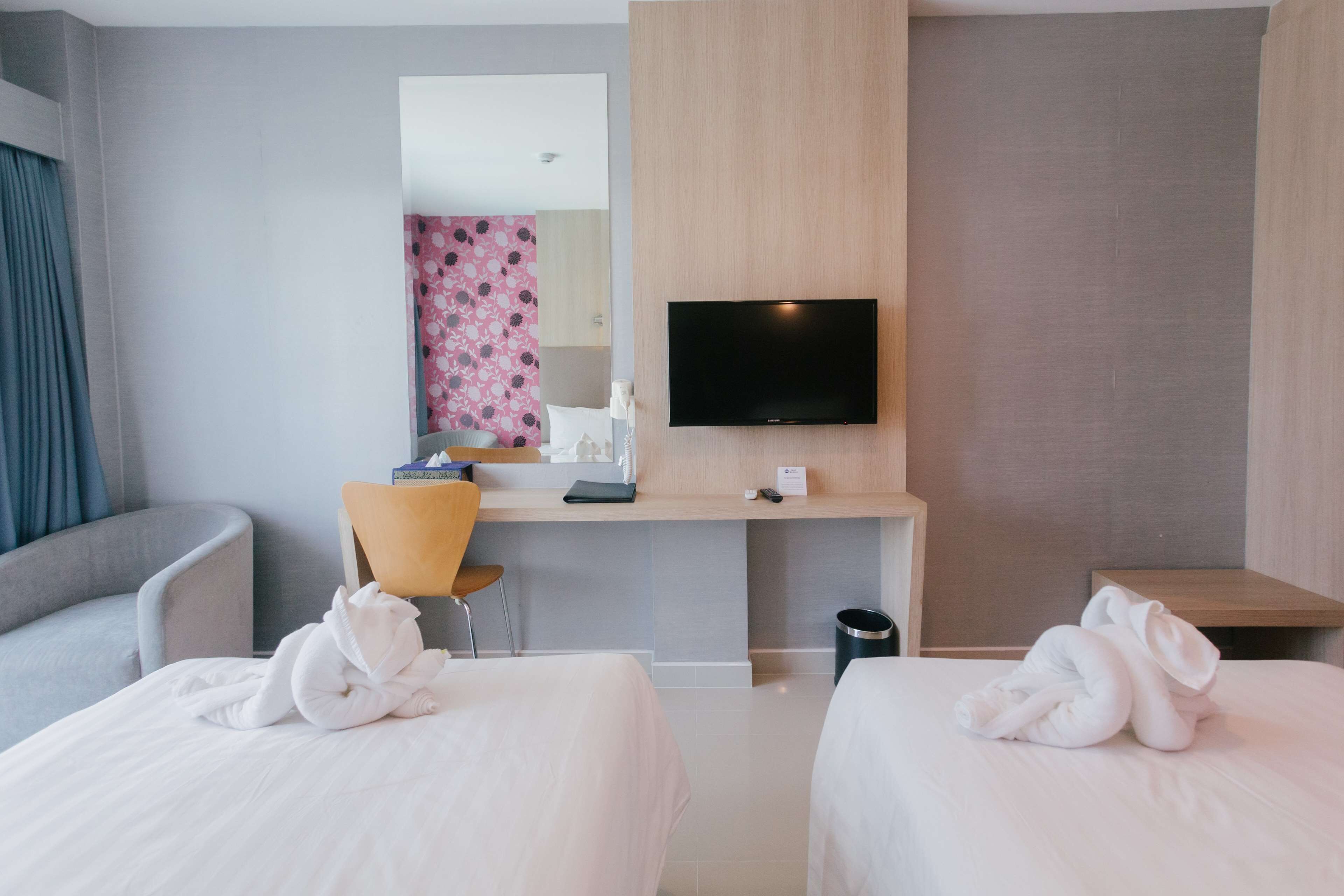 Una habitación de hotel con dos camas, un escritorio con una silla, un televisor de pantalla plana y un espejo.