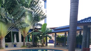 Un área de comedor junto a la piscina con una mesa preparada para dos, rodeada de palmeras y una piscina azul cristalina.