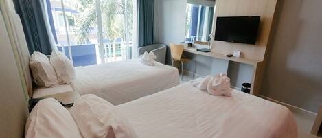 A hotel room with two beds, a TV, a desk, and a view of the outdoors.