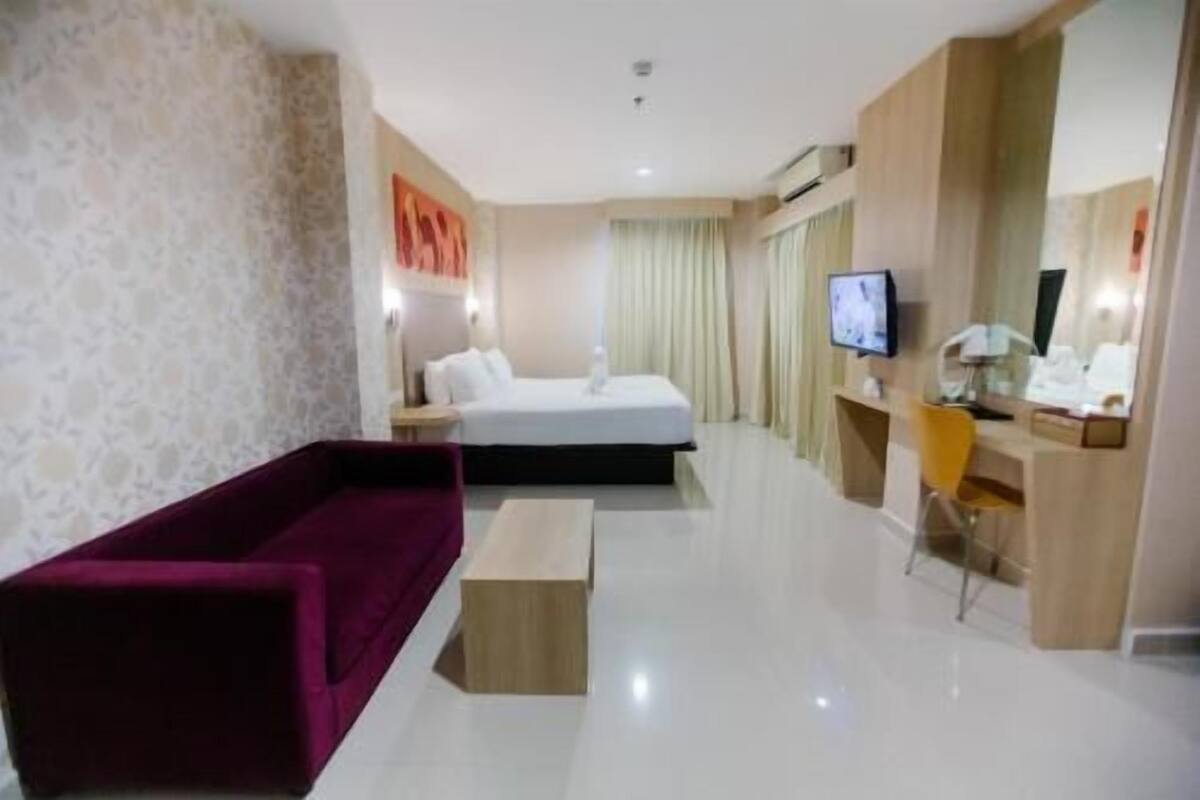 Habitación de hotel con cama, sofá, escritorio con silla, televisión y espejo.