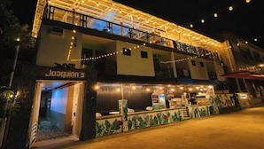 Un edificio de dos pisos con un restaurante llamado 'Joaquinn's' en la planta baja, que cuenta con un balcón con guirnaldas de luces.