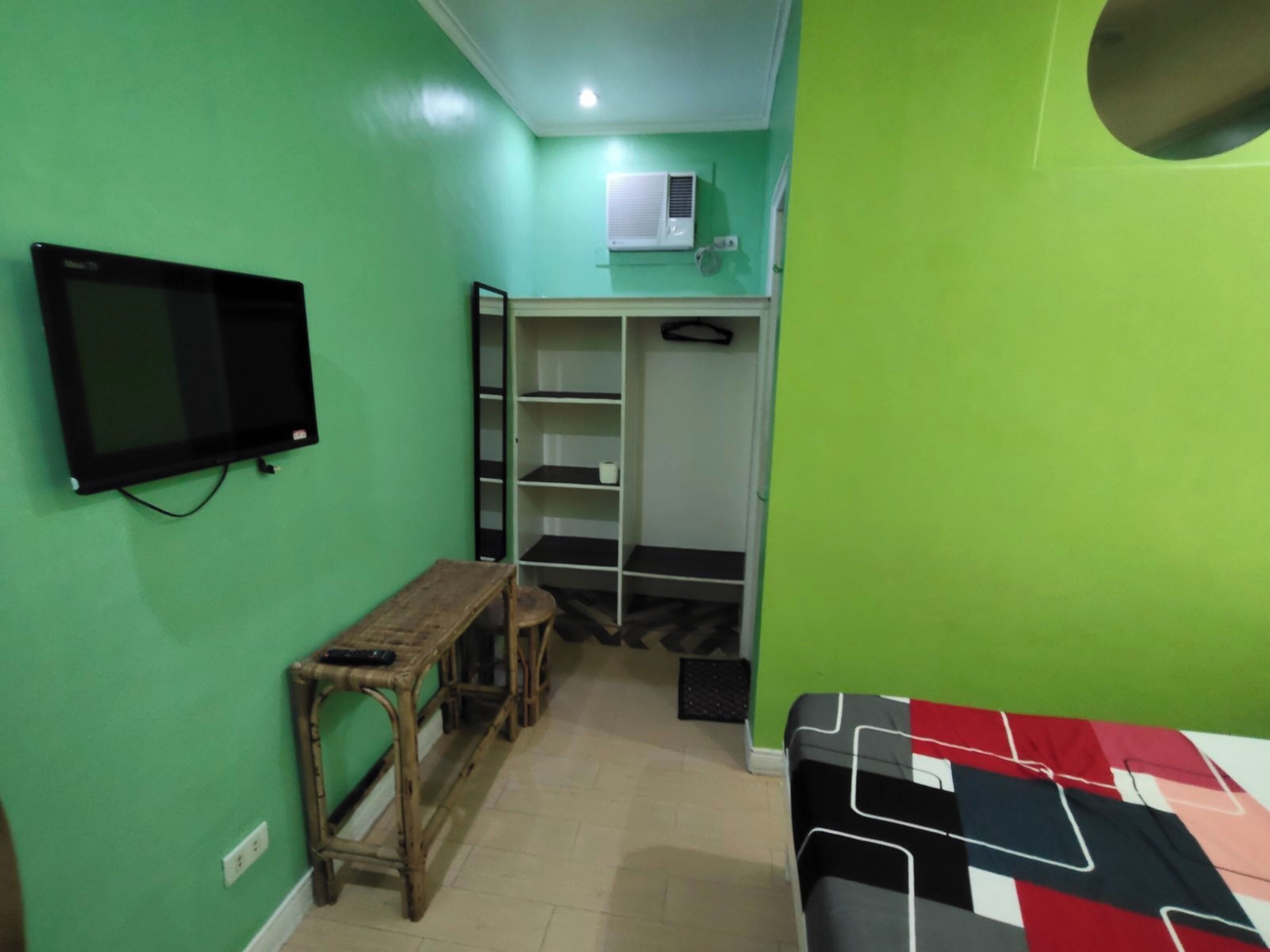 Een kamer met een bed, een bureau, een stoel, een televisie, een kledingkast en een airconditioning.