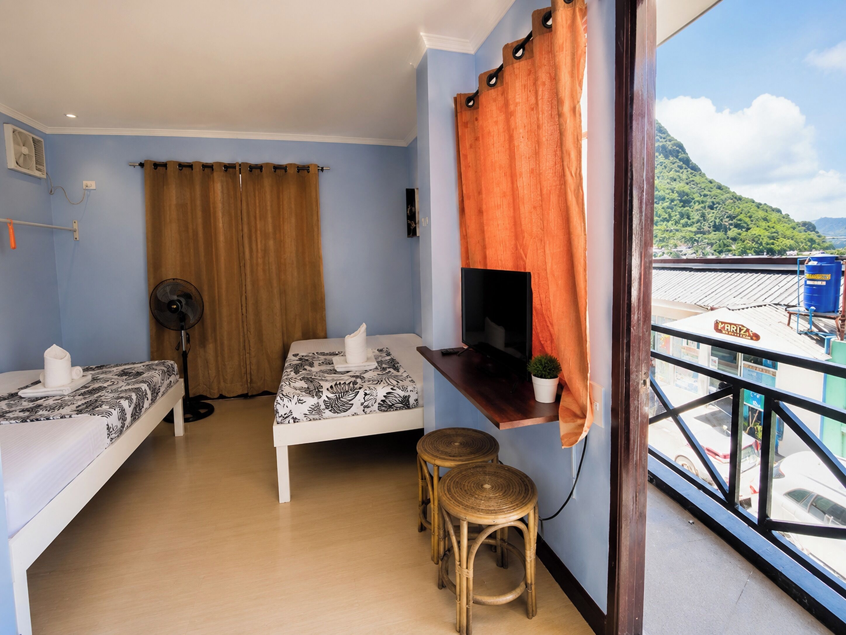 A hotel room with two beds, a TV, a fan, and a balcony with a view of a mountain.