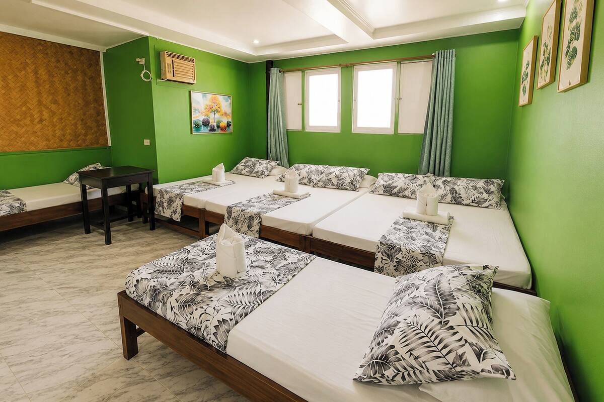 A hotel room with four single beds, a wooden bench, a small table, and a painting on the wall.