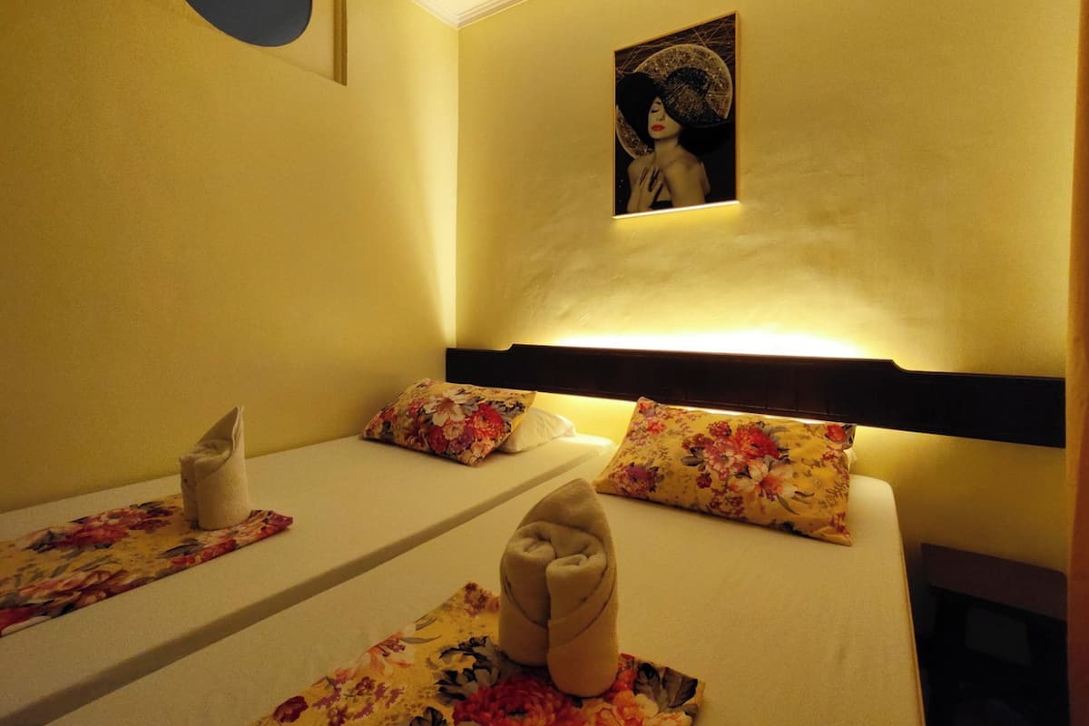 Habitación de hotel con dos camas, cada una con almohadas estampadas con motivos florales y una toalla doblada con cuidado.