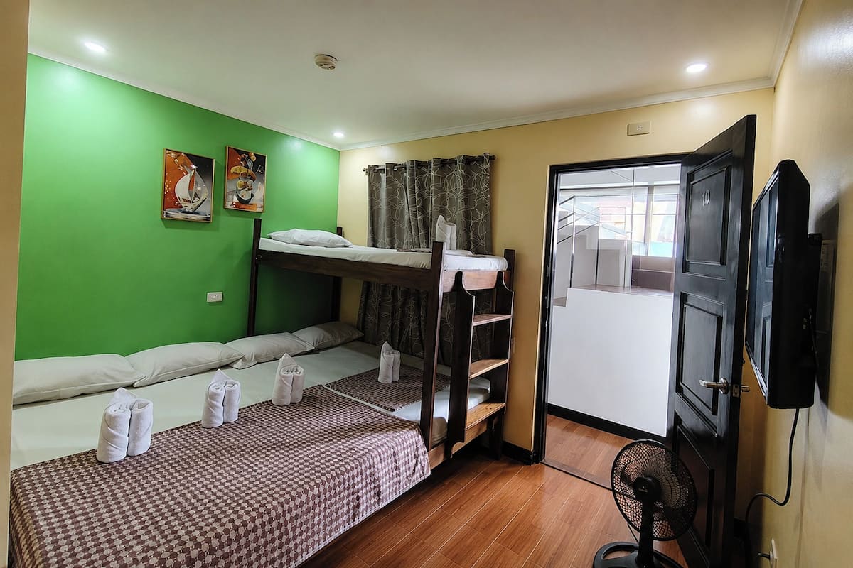 A room with bunk beds, a fan, a television, and a door leading to another room.