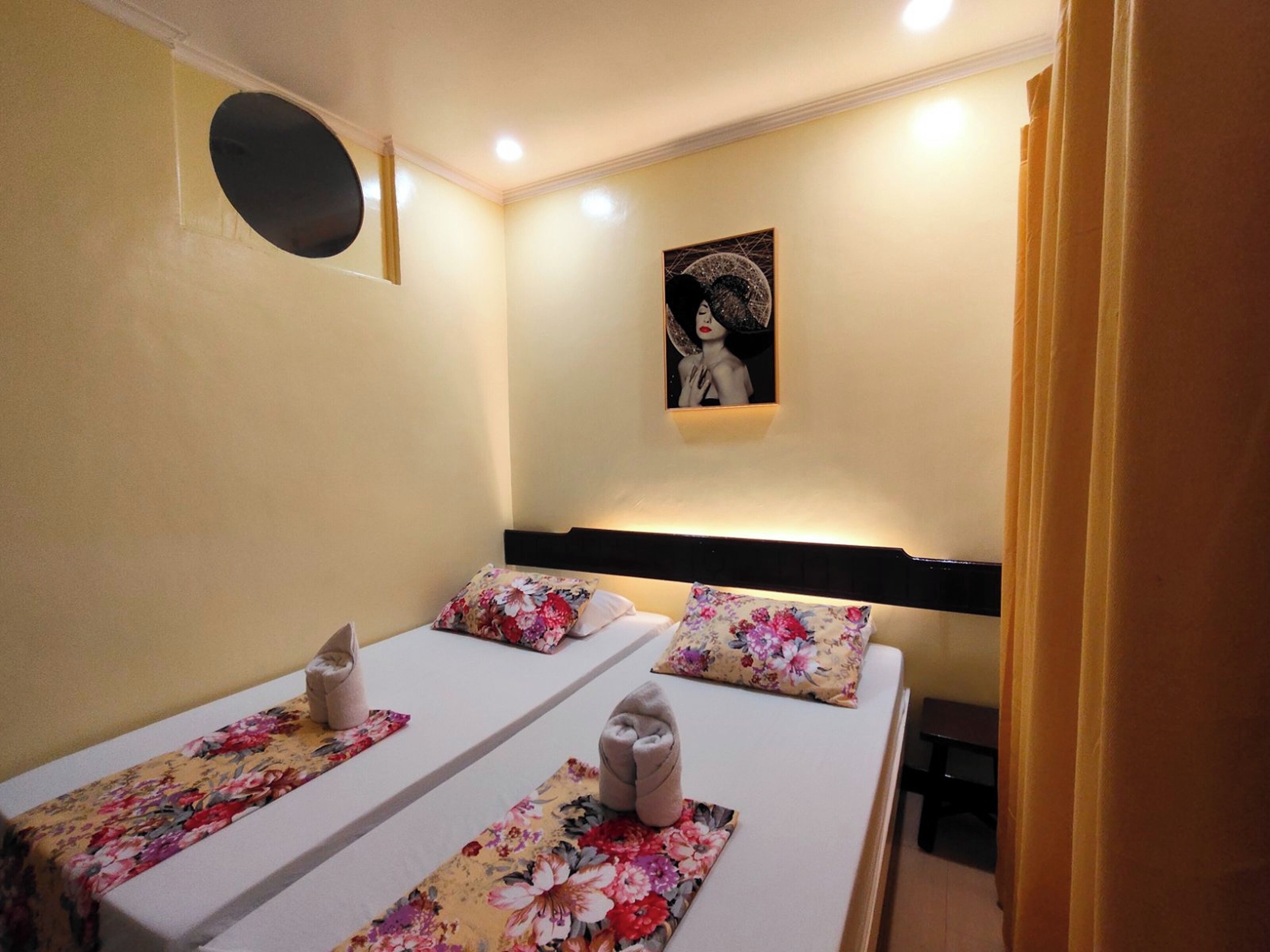 Una habitación de hotel con dos camas, cada una con ropa de cama floral y cabecero. Hay un cuadro en la pared y una pequeña ventana circular.