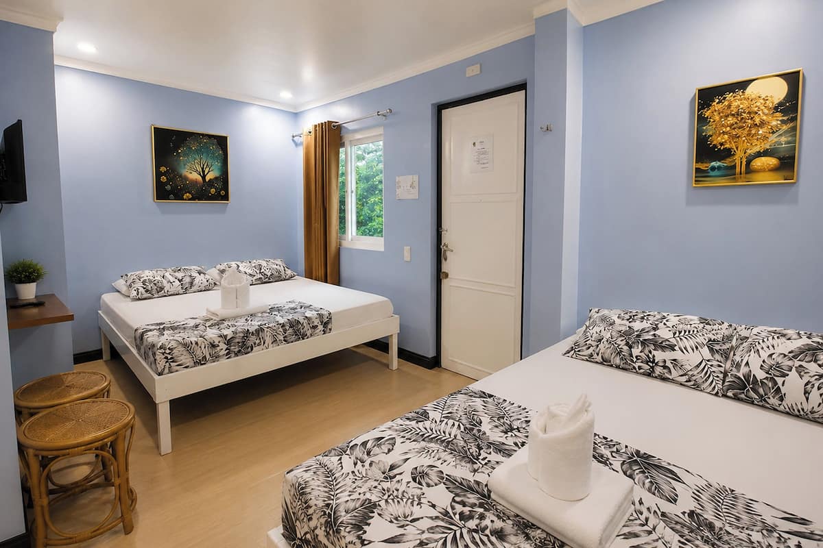 A hotel room with two beds, a television, a window with curtains, and artwork on the walls.