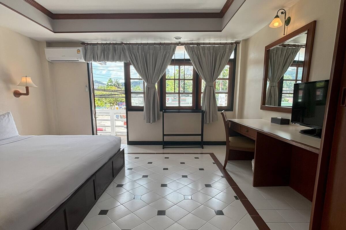 A hotel room with a bed, a desk, a TV, and a window with curtains.