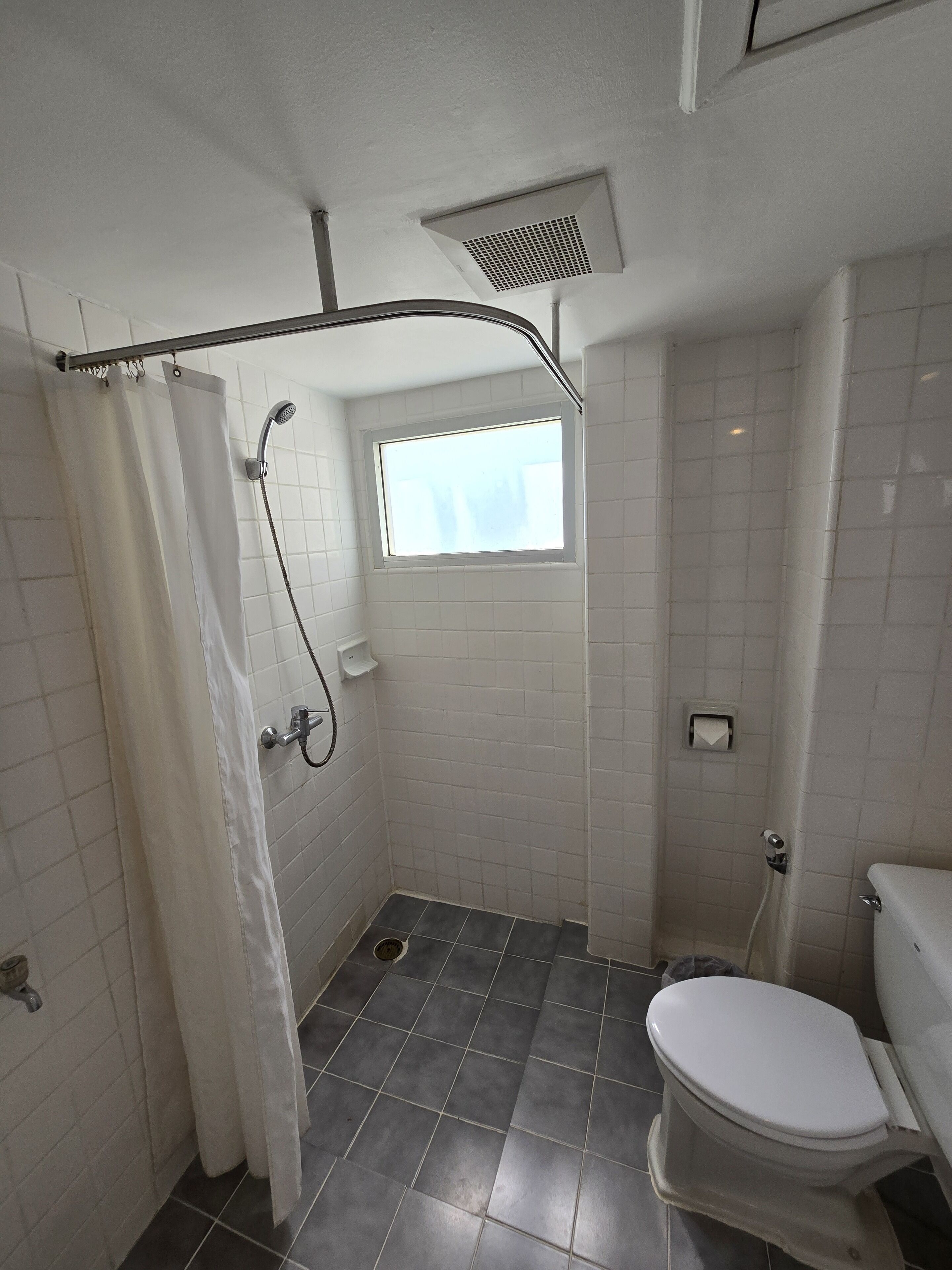 A small, tiled bathroom with a shower, a window, and a toilet.