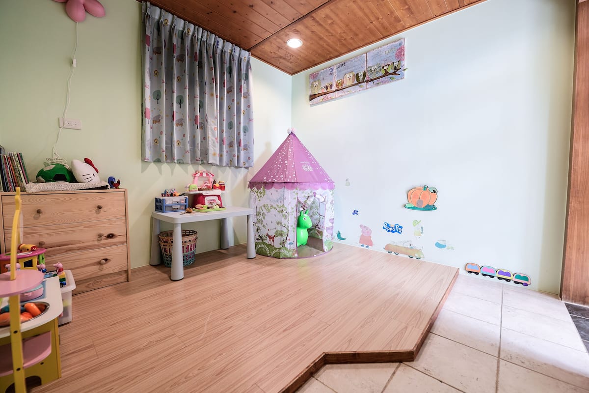 Ein Kinderzimmer mit Holzboden, einem rosa Spielhaus und verschiedenen Spielzeugen.