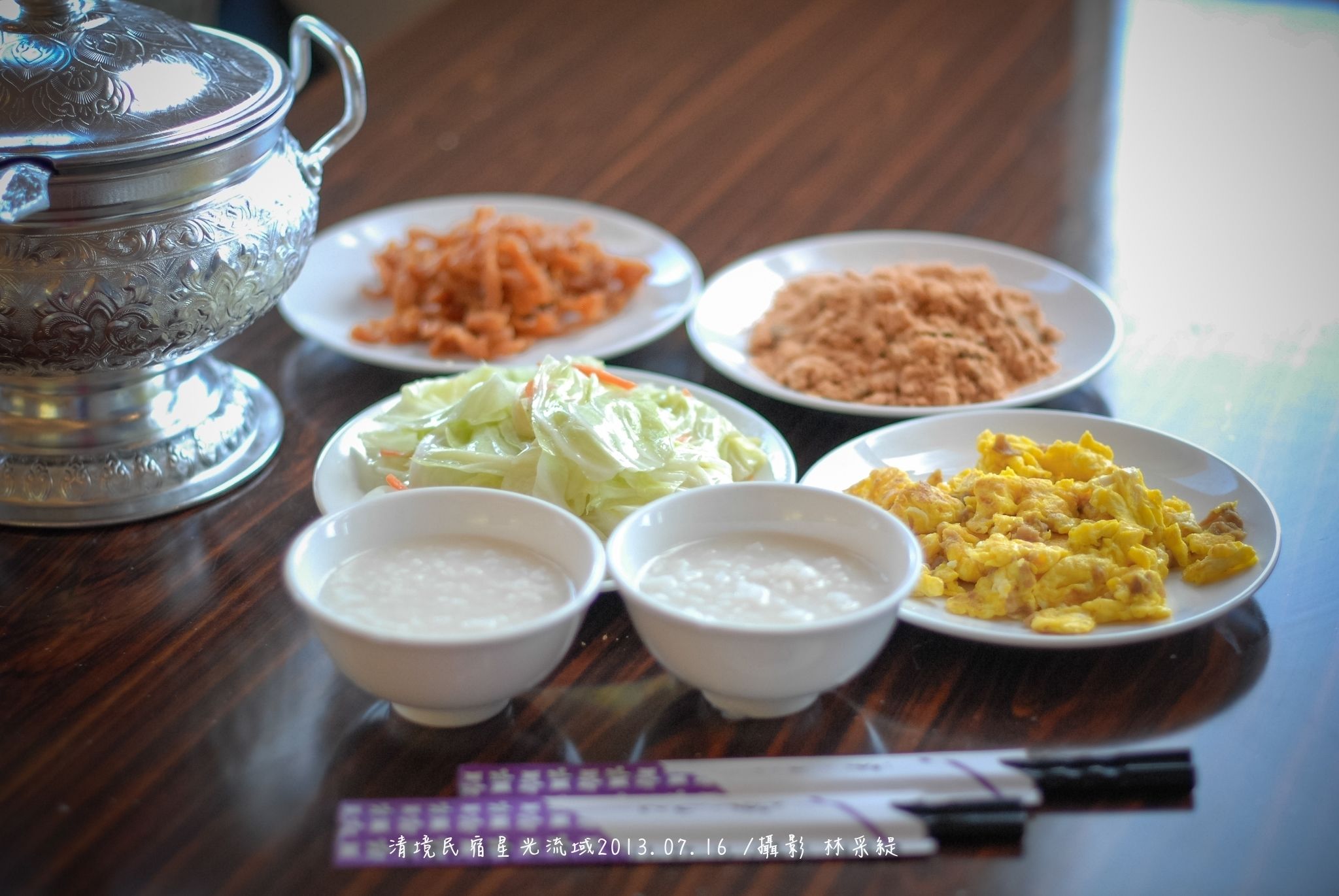 Una mesa con diferentes platos, incluyendo una olla de plata, fuentes de comida y tazones de sopa.