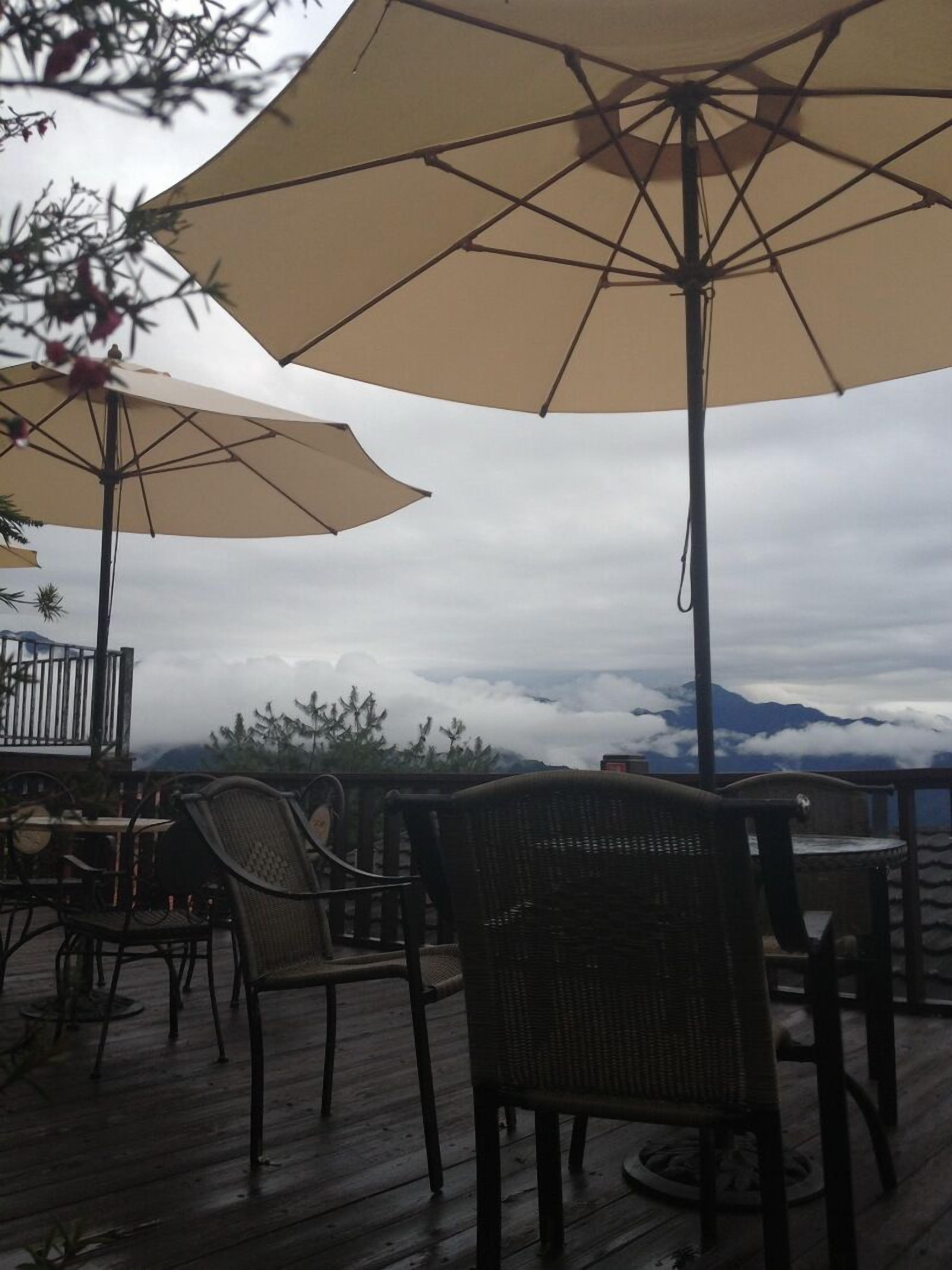 An outdoor patio with wicker chairs and large beige umbrellas, overlooking a mountainous landscape.