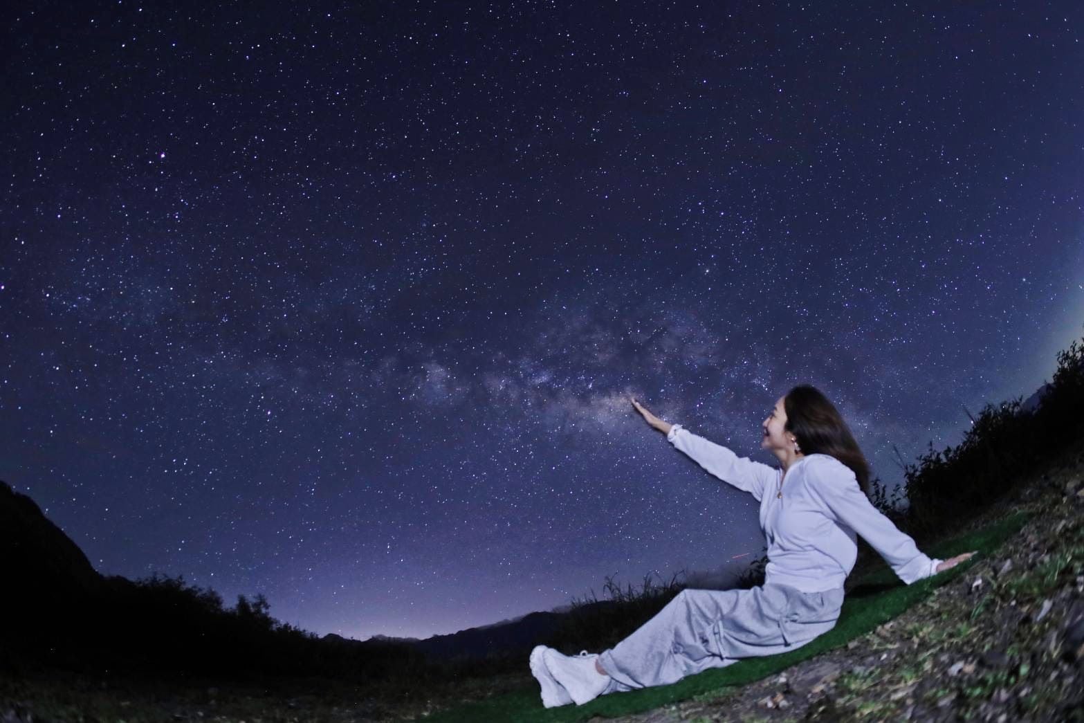 A person sitting on a grassy slope under a starry night sky.