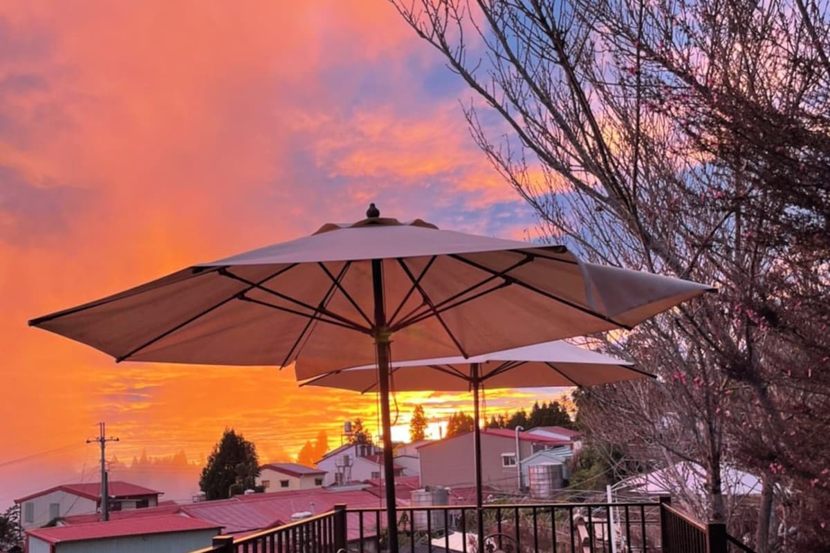 Une terrasse en bois, agréée de mobilier d’extérieur et d’un grand parasol, d’où l’on peut admirer un quartier résidentiel au coucher du soleil.