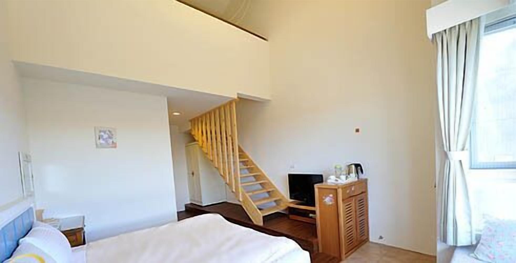 A hotel room with a bed, a wooden staircase, a television, and a small cabinet.