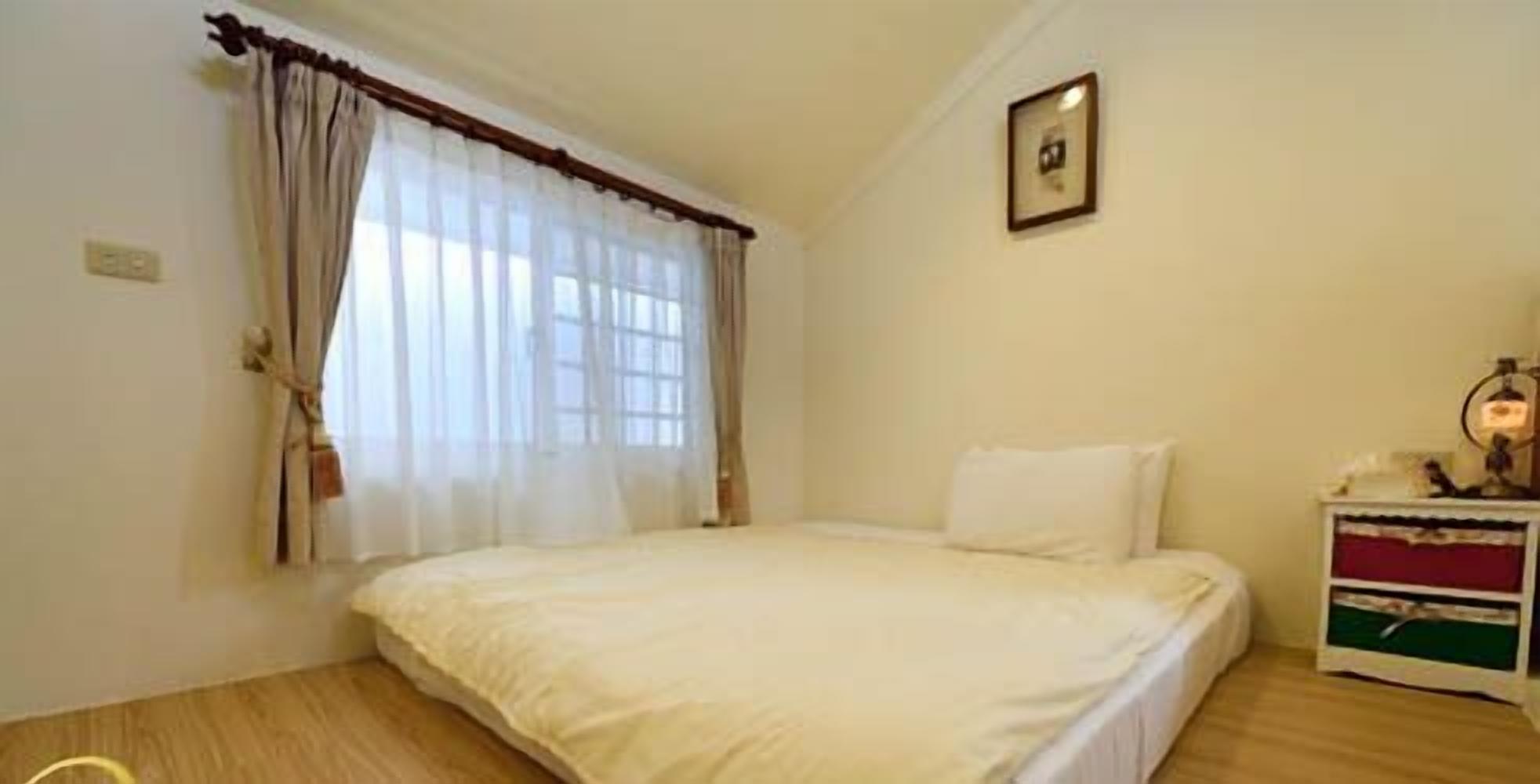 A bedroom with a bed, a nightstand, a lamp, and a window with curtains.