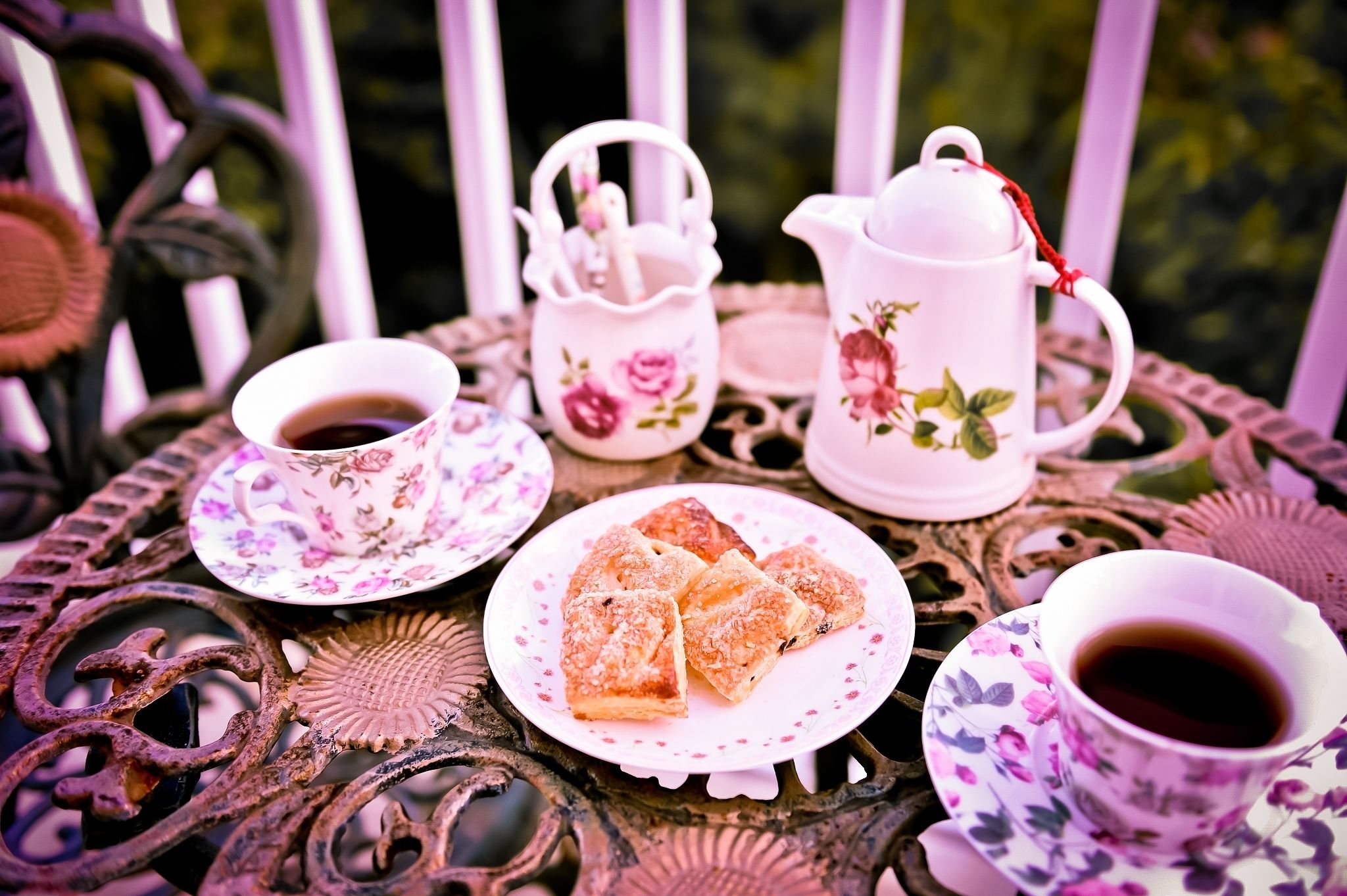 Una mesa con una tetera floral, tazas y pasteles.