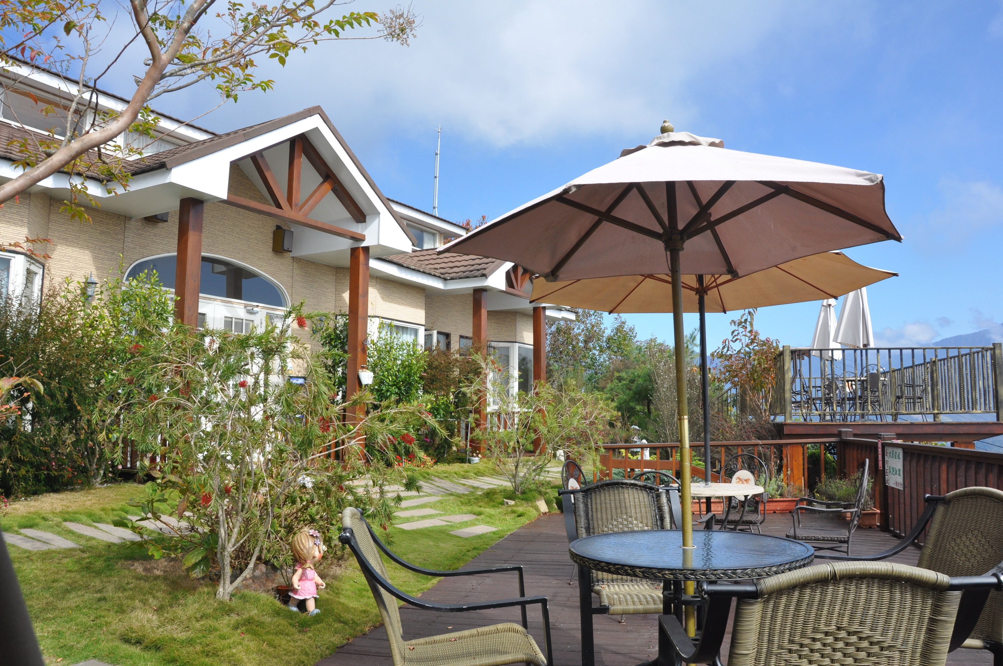 En patio med udendørs møbler, en stor parasol og udsigt til et hus med en terrasse.