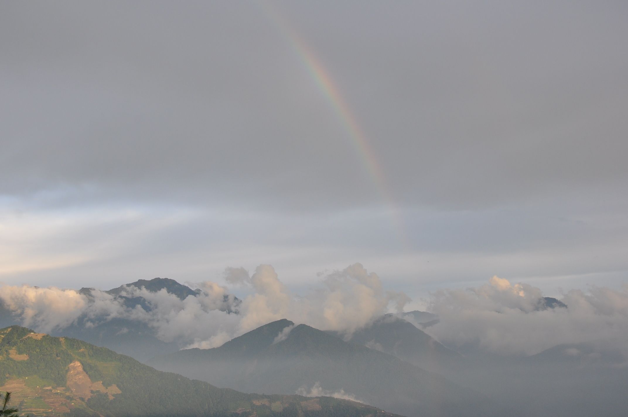 A mountain landscape with a rainbow and clouds.