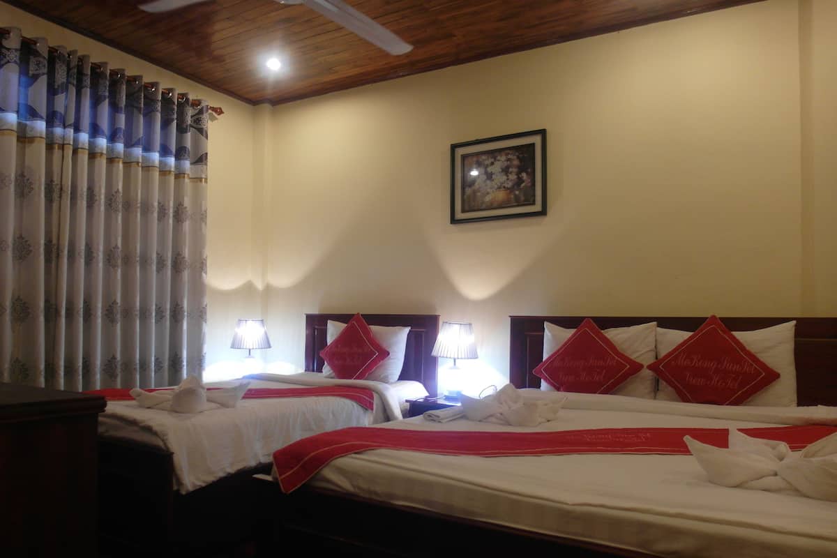 A hotel room with two beds, each with red pillows and white linens. There are two bedside lamps and a ceiling fan.