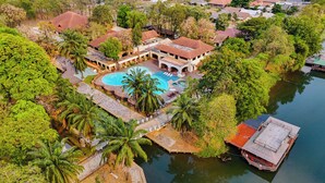 An aerial view of a resort with a swimming pool, palm trees, and a dock.
