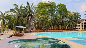 A swimming pool with a hot tub, lounge chairs, and palm trees.