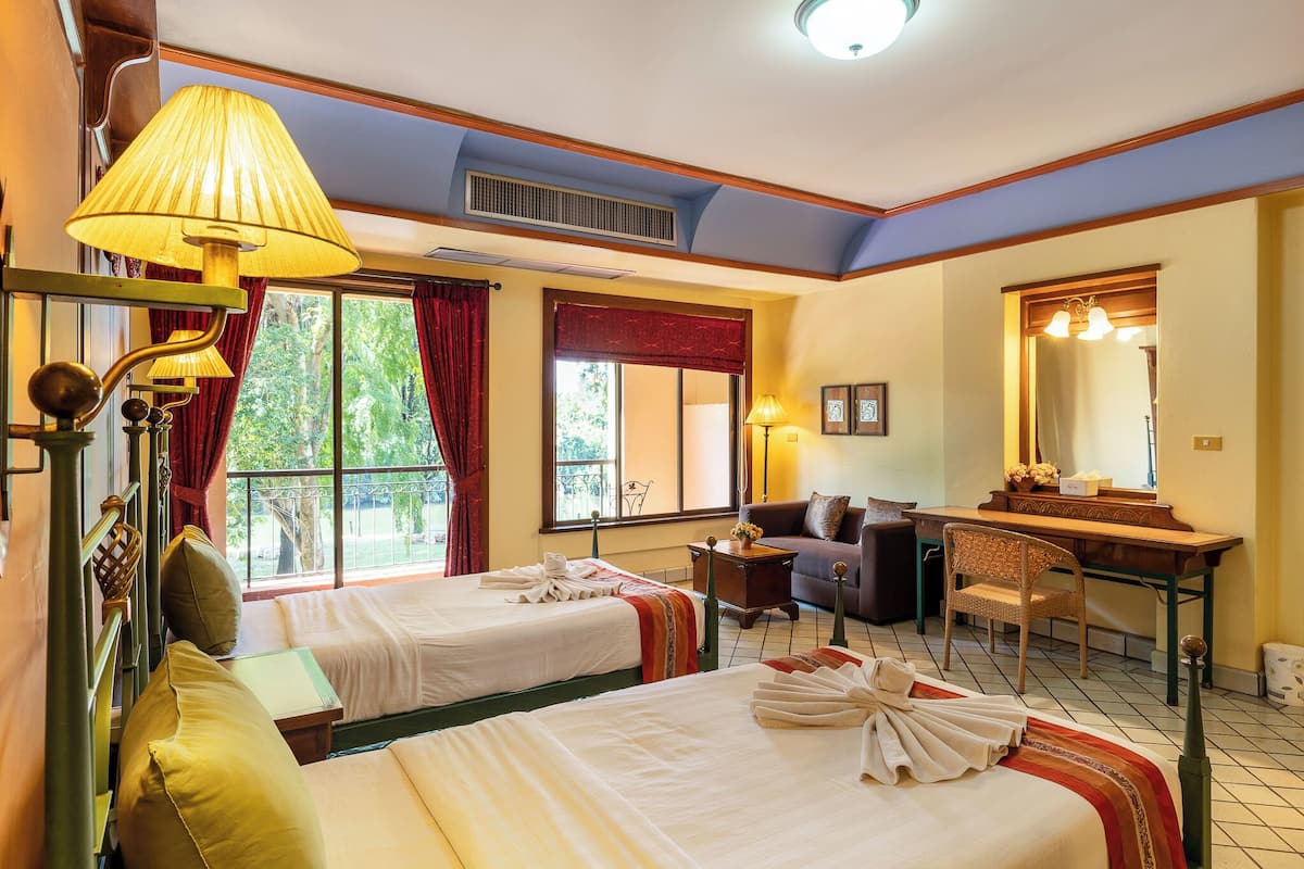 A hotel room with two beds, a desk, a chair, a sofa, and a large window with curtains.