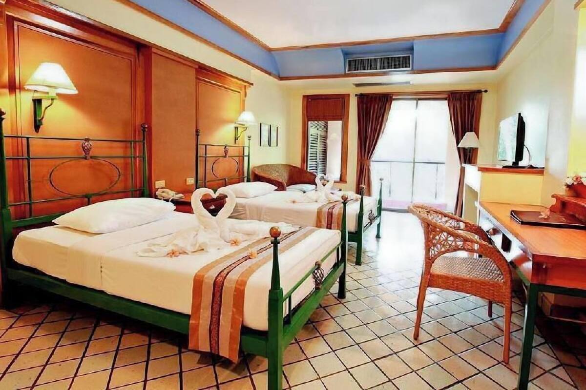 A hotel room with two beds, a desk, a chair, a TV, and a window.