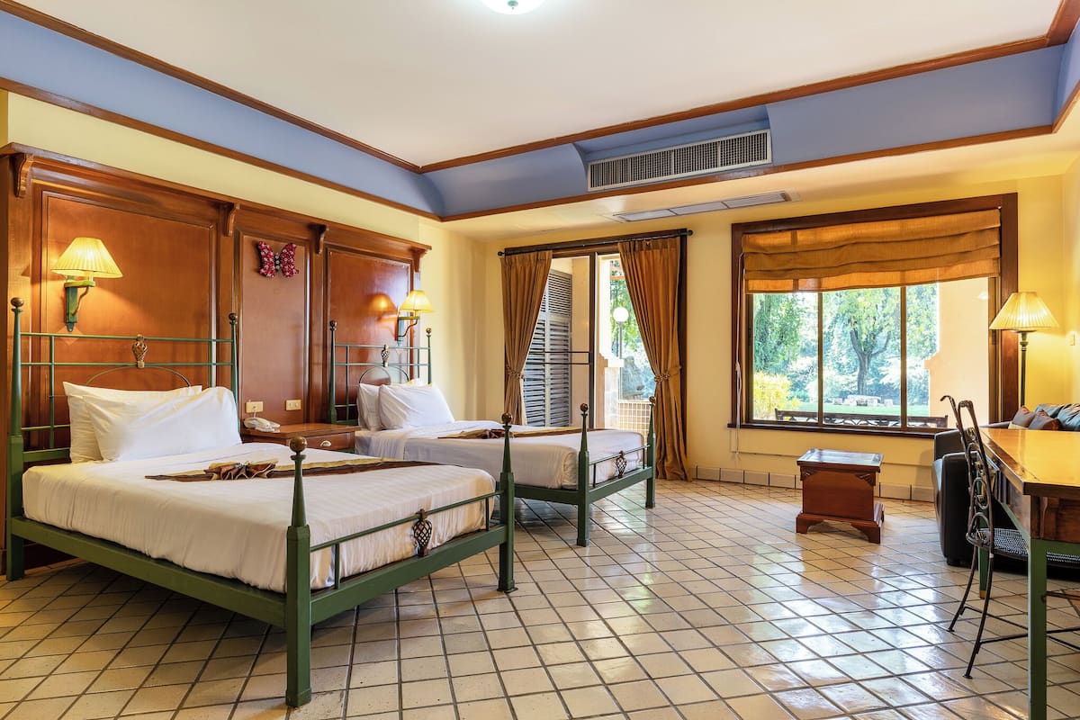 A hotel room with two beds, a small table, a chair, and a window with curtains.