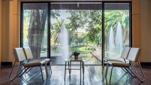 A room with a large sliding glass door leading to a garden with a fountain, two chairs, and a small table with a plant.