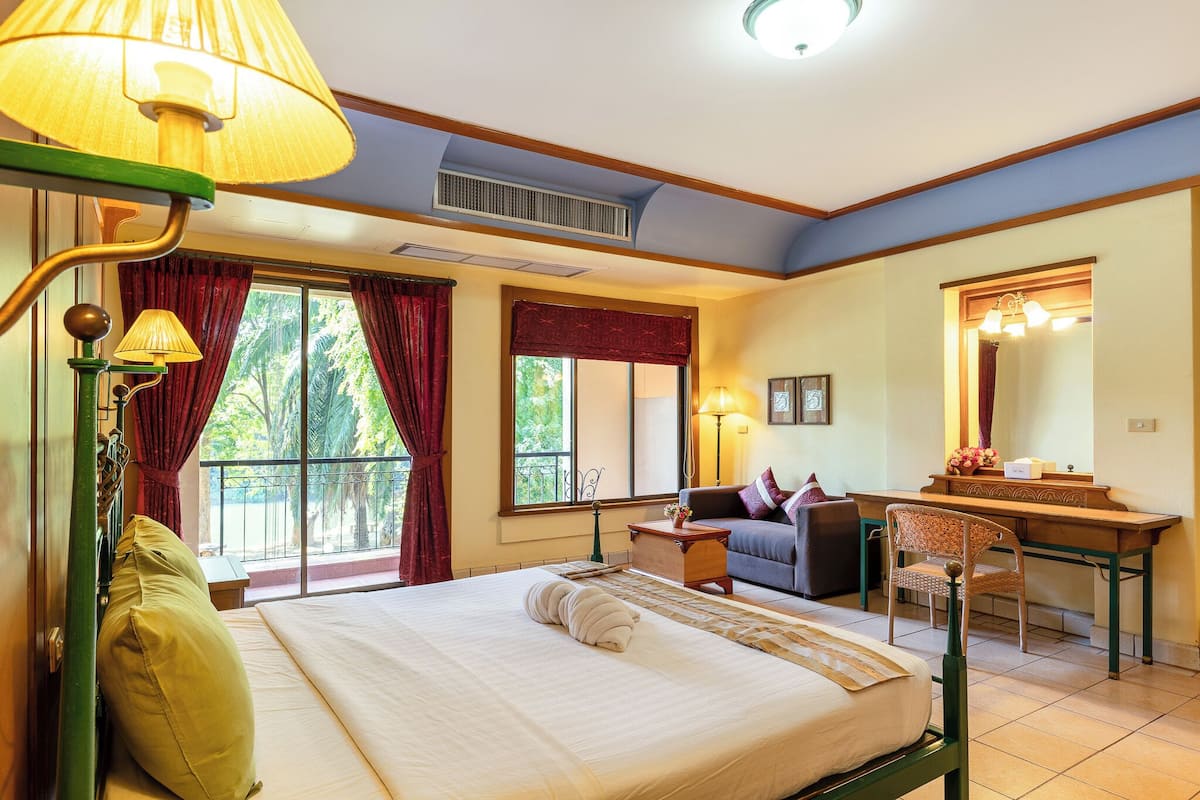A hotel room with a bed, a desk, a chair, a lamp, a window with curtains, and a balcony.