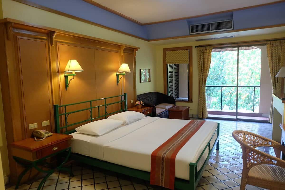 A hotel room with a bed, bedside lamps, a telephone, a chair, a window with curtains, and a view of greenery.