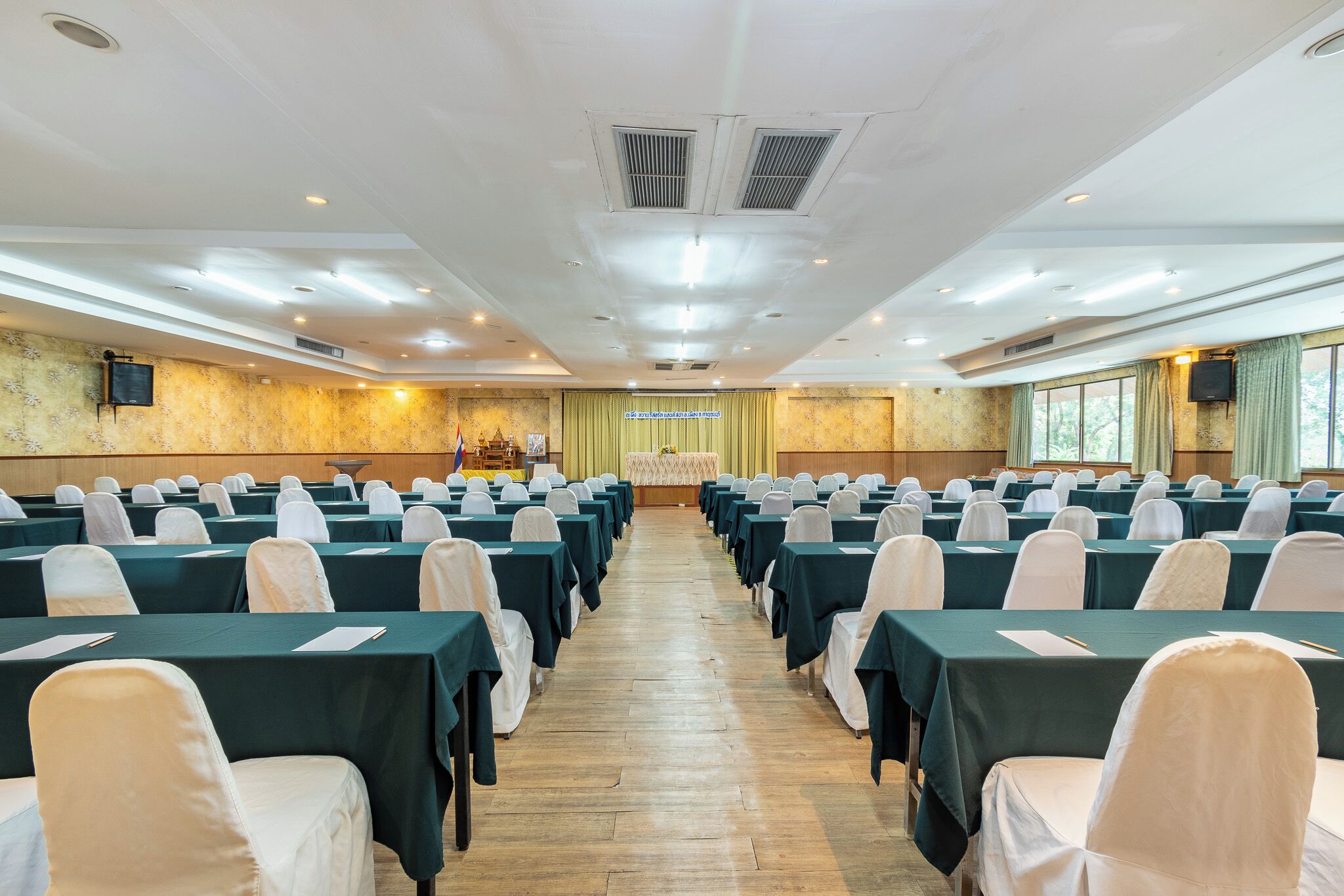 Une salle de conférence avec des rangées de tables et de chaises, un pupitre et une grande fenêtre.