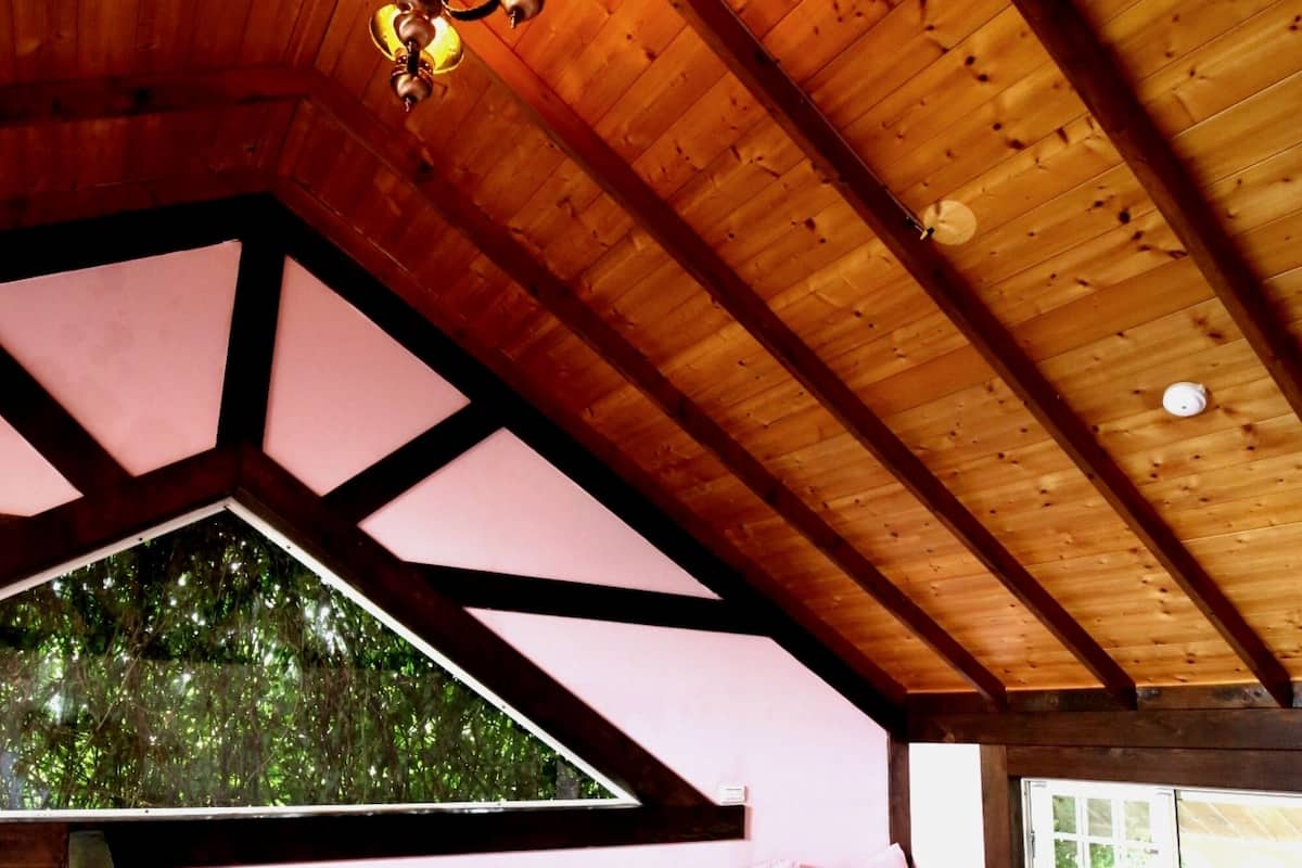 A cozy attic bedroom with a wooden ceiling, two beds with floral bedding, and a chandelier.