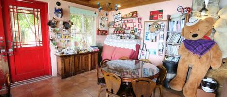 Un comedor acogedor con una puerta roja, un oso de peluche grande y una estantería llena de libros y adornos.