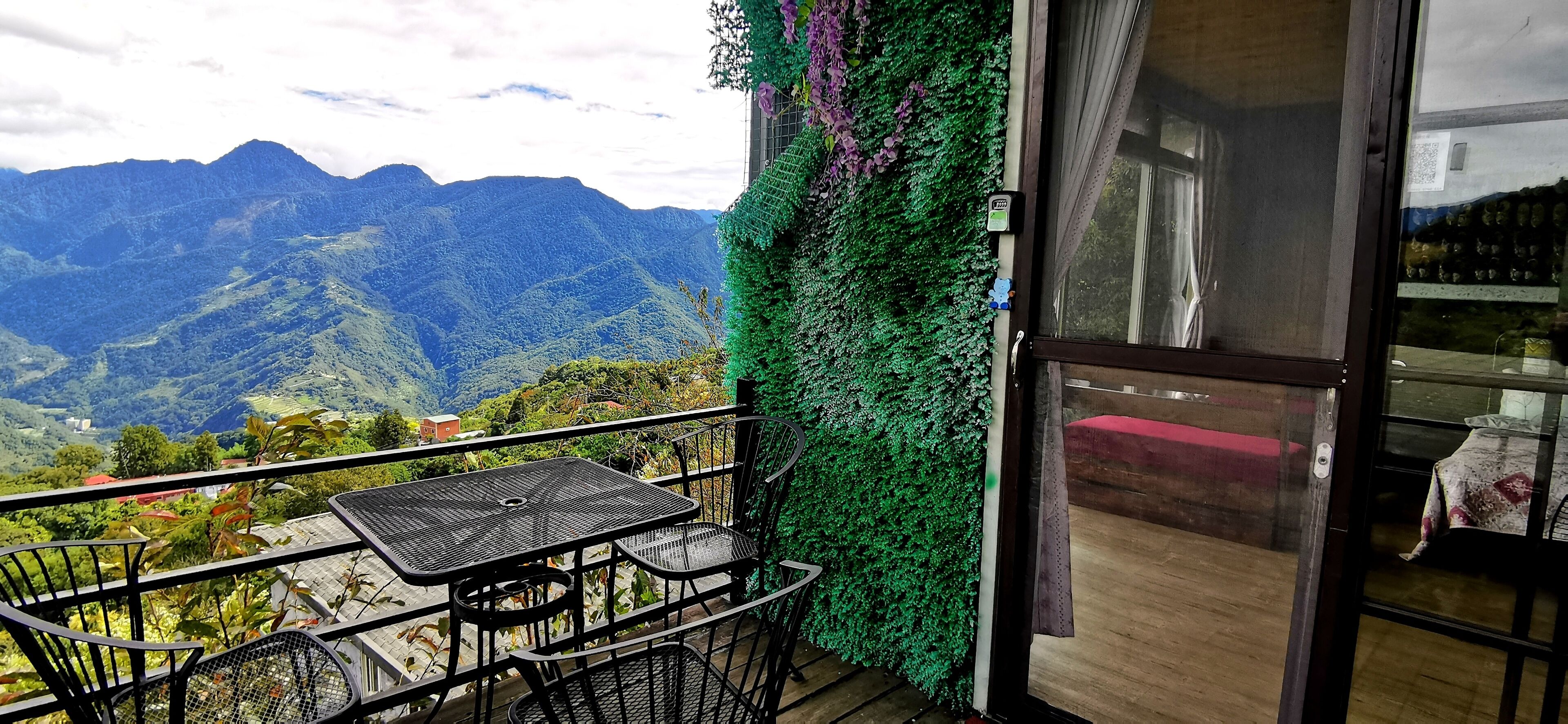 Un balcon avec une table et des chaises, une vue sur les montagnes et un mur végétal.