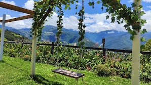 Una pérgola de fusta amb enfiladera, un balancí i vistes a les muntanyes.