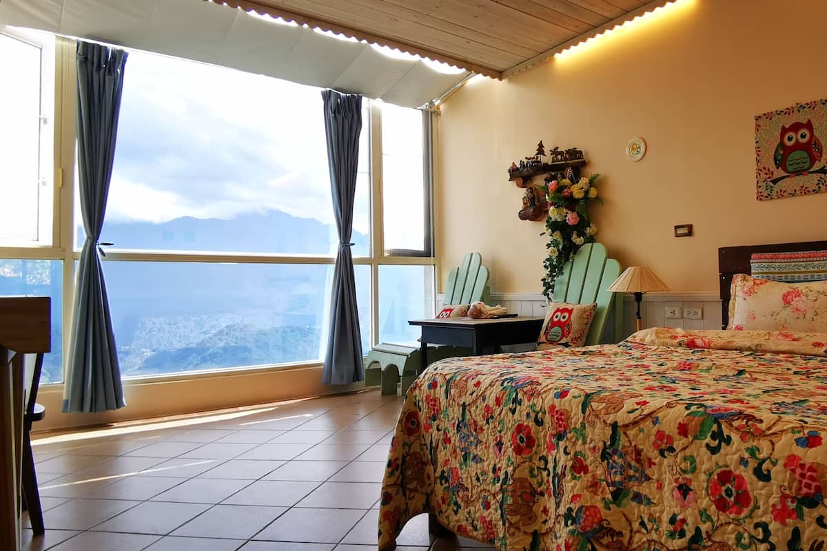 A room with a large bed, a view of mountains, and a window with curtains.
