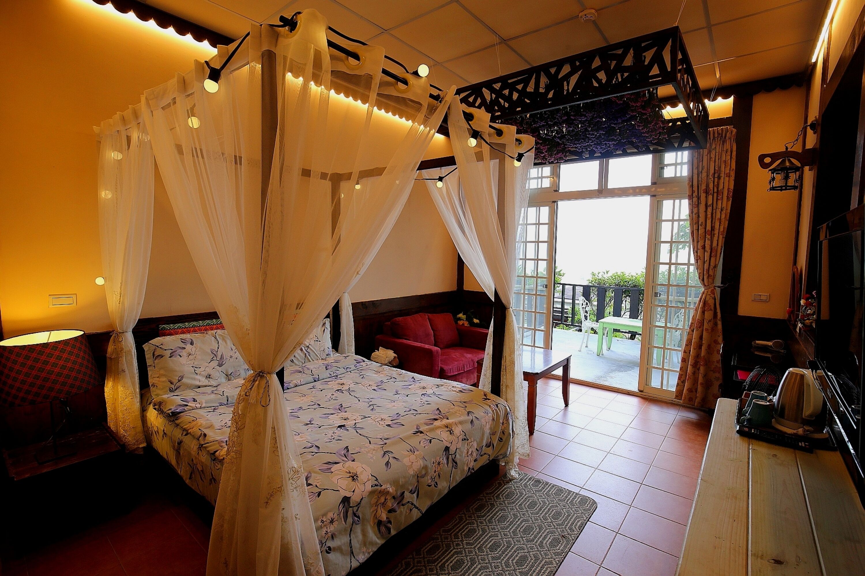 A bedroom with a four-poster bed, a red chair, and a balcony with a table and chairs.