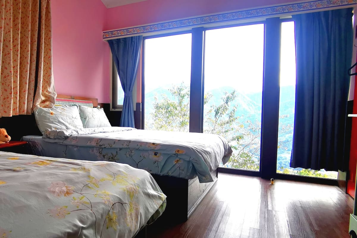 A bedroom with two beds, a nightstand, and a window with curtains.